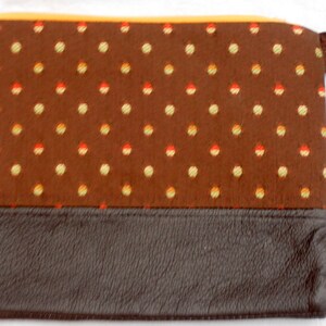 May include: A brown fabric zippered pouch with a brown leather bottom and a yellow fabric lining. The fabric has a polka dot pattern with small yellow, orange, and red dots.