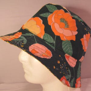 May include: A black bucket hat with a floral print featuring pink, orange, and yellow flowers on a dark green background.