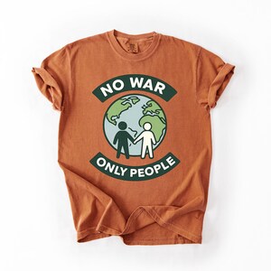 May include: Burnt orange t-shirt with the text "NO WAR ONLY PEOPLE" in green and white. The graphic features a globe with two figures holding hands. The shirt has short sleeves and a crew neck.