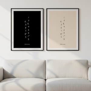 Puede incluir: Dos impresiones artísticas enmarcadas con fondos negros y beige. Cada impresión presenta una disposición vertical de números y letras, con el texto "Where we met" en la parte inferior. Los marcos son negros y las impresiones se muestran sobre un sofá blanco.
