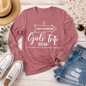 May include: A mauve long-sleeve shirt featuring a white graphic of a directional sign with the text TRIP DESTINATION, Girls Trip, 2026, and the phrase GREAT TIMES GREAT LAUGHS GREAT MEMORIES printed in a clean, white, sans-serif and script font.