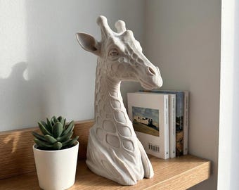 May include: A matte off-white giraffe bust sculpture featuring a detailed textured pattern of spots across the neck and head, with prominent ossicones and ears, positioned as a decorative figurine with a smooth, solid finish.