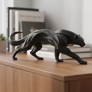 May include: A black panther sculpture with a sleek, modern design. The sculpture is positioned on a wooden surface, with books and a small potted plant in the background. The panther is depicted in a walking pose.