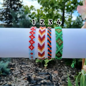 Pode incluir: Quatro pulseiras da amizade tecidas rotuladas 1, 2, 3 e 4. A pulseira 1 tem um padrão de diamante vermelho e azul claro. A pulseira 2 apresenta um design de chevron em laranja, vermelho e branco. A pulseira 3 tem listras pretas, laranjas e azuis. A pulseira 4 é verde.