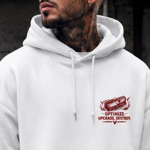 May include: A white long-sleeve hooded sweatshirt featuring a front kangaroo pocket and a small graphic on the left chest. The graphic depicts a red mechanical component with the text "OPTIMIZE. UPGRADE. DESTROY." printed in red capital letters.