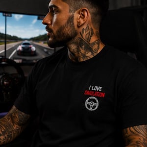 Könnte beinhalten: Ein schwarzes kurzärmeliges T-Shirt mit einer Grafik auf der Brust. Die Grafik enthält den Text "I LOVE" in Weiß, "SIMULATION" in Rot und eine weiße Strichzeichnung eines runden Lenkrads, die unter dem Text platziert ist.