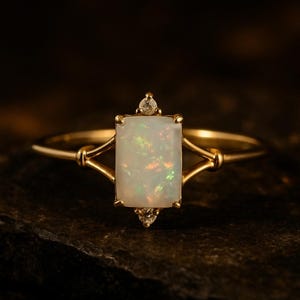 May include: A gold ring featuring a rectangular opal gemstone with iridescent flashes of color. Two small diamonds are set above and below the opal. The ring has a delicate, openwork design.
