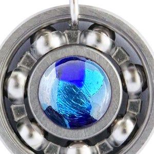 May include: Silver pendant necklace with a circular design and a blue glass centre. The pendant has a mechanical bearing appearance, with small silver balls around the blue glass. The necklace chain is made of small silver beads.