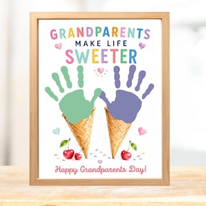 May include: A framed print featuring the text GRANDPARENTS MAKE LIFE SWEETER and Happy Grandparents Day. The design includes two ice cream cones topped with green and purple handprints, small watercolor hearts, and red cherries at the bottom.