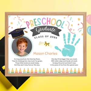 May include: A framed preschool graduation keepsake with a photo of a child, a handprint, and the text "Preschool Graduate Class of 2026." The frame is light brown, and the background is white with colorful accents.
