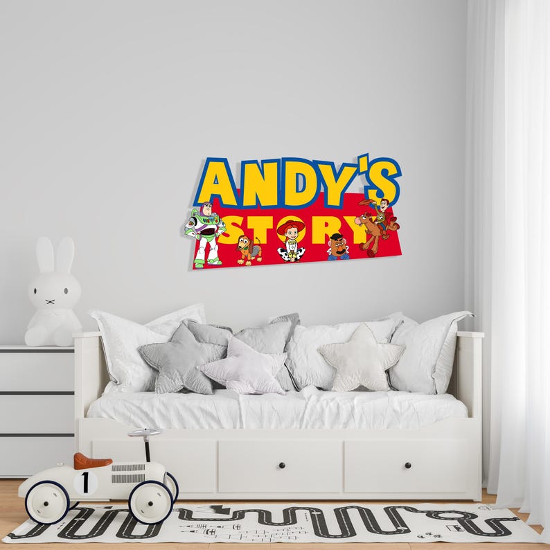 K&ouml;nnte beinhalten: Wanddekoration mit dem Text "ANDY'S STORY" in Gelb und Blau, mit Charakterillustrationen. &Uuml;ber einem wei&szlig;en Bett mit grauen sternf&ouml;rmigen Kissen. Ein wei&szlig;es Spielzeugauto und eine Hasenlampe befinden sich im Vordergrund.