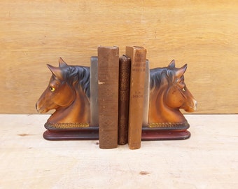 May include: A pair of brown horse head bookends holding up three books. The book on the right is titled "The Great Airport Mystery" by F.W. Dixon.