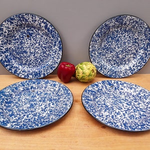 May include: Four blue and white speckled enamel dinner plates with black rims. The plates are arranged in a square pattern on a wooden surface.