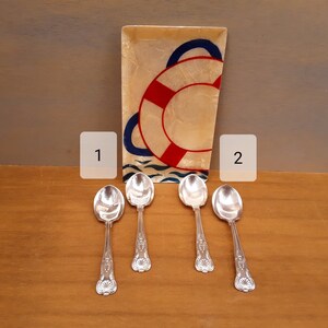 May include: Four silver spoons with ornate handles on a wooden surface. A decorative tray with a nautical theme is in the background.