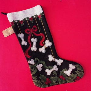 May include: Black Christmas stocking with white bone and red ribbon design. The stocking has a white cuff and is decorated with holly and berries. A tag is attached to the stocking.