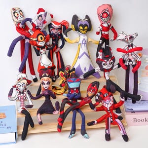 May include: A collection of plush dolls featuring various characters. The dolls have elongated limbs and detailed facial features, with a variety of colors including red, black, white, and purple. They are arranged on a wooden display.