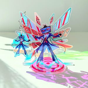 Może przedstawiać: Holograficzny akrylowy brelok przedstawiający postać z kreskówki z głową w postaci ekranu telewizora, ubraną w niebieski garnitur i koszulę w czerwone paski. Brelok ma duży, ozdobny, skrzydlaty wzór i mocowanie do kluczy.