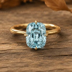 May include: A gold ring with a large, rectangular, light blue gemstone. The ring is set on a wooden surface with a blurred background. The gemstone is the focal point, showcasing its clarity and color.