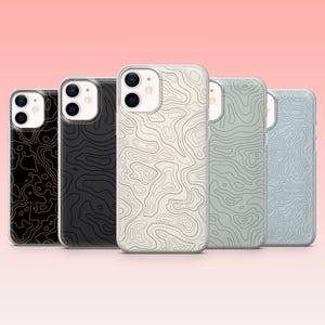May include: Five iPhone cases featuring a topographic map design in different colours: black with gold lines, solid black, off-white with dark lines, light grey with dark lines, and light blue with dark lines. Set against a pink backdrop.