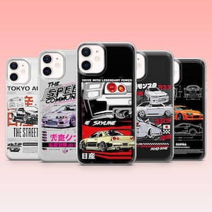 May include: A collection of phone cases featuring car designs. The cases display illustrations of various vehicles, including a white car with the text "IE SKYLINE" and a yellow car with the text "日産". Other cases have text like "TOKYO AI" and "THE STREET".