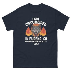 May include: Navy blue t-shirt featuring the text "I GOT CIRCUMCISED IN EUREKA, CA BEHIND THE BOWLING ALLEY" and a wolf graphic with flames. An infinity symbol is below the text.