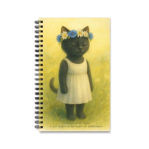 May include: Spiral-bound notebook featuring a whimsical illustration of a black cat wearing a flower crown and a white dress. The cat is set against a yellow background with the text "Summer never ends, it just lingers in the scent of wildflowers."