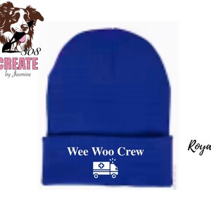 Könnte beinhalten: Königsblauer Beanie mit dem Text "Wee Woo Crew" und einer weißen Krankenwagen-Grafik. Der Beanie hat einen umgeschlagenen Saum und eine einfarbige Farbe. Das Bild enthält auch das Wort "Royal" in Schreibschrift.