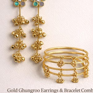 May include: Gold-toned jewelry set featuring earrings and bracelets. The earrings have flower-shaped tops with colorful accents and dangling bells. The bracelets are gold bangles with floral charms. The text reads "Gold Ghungroo Earrings & Bracelet Combo".