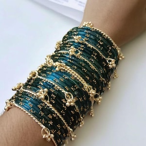 May include: A stack of teal and gold bangles. The bangles are a deep teal color with gold accents and small dangling gold charms. The bangles are stacked on top of each other, creating a layered effect. The gold accents include a twisted rope design and small gold beads.