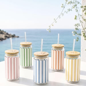 May include: Five clear glass tumblers with bamboo lids and clear plastic straws. Each tumbler features vertical stripes in a different pastel color: light pink, green, light blue, peach, and yellow. The glasses have a cylindrical shape.
