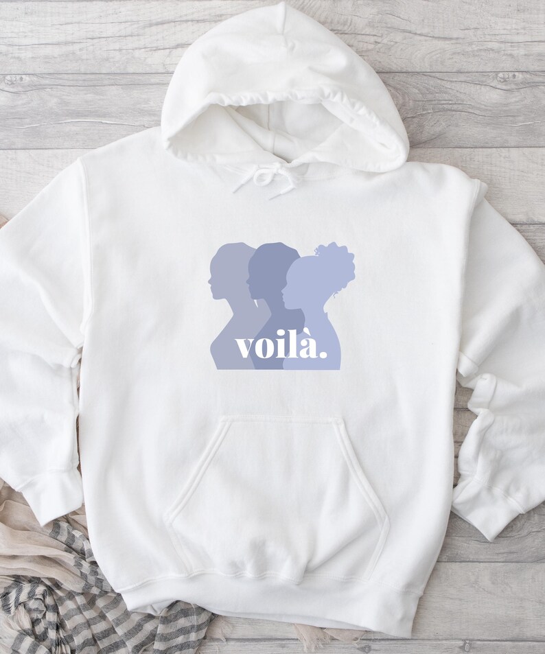 May include: White hooded sweatshirt with a front pocket and drawstring. The front features a design of three women's silhouettes in shades of purple, with the word "voil&agrave;" in a matching purple font.