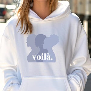 May include: White hoodie with a front graphic of three women's silhouettes in shades of blue, with the word "voil&agrave;" in a stylized font. The hoodie has a drawstring hood and a front pocket.