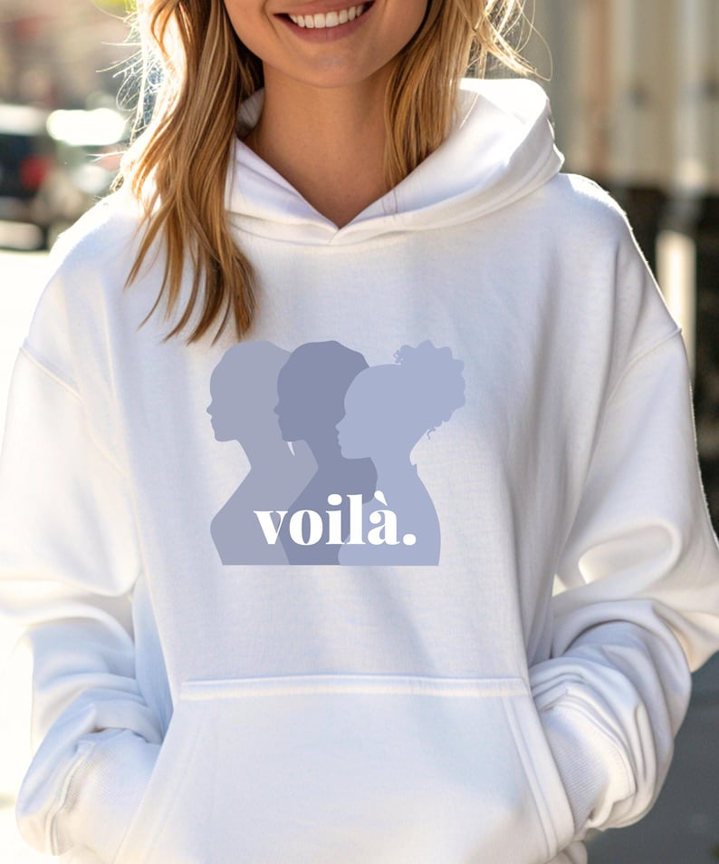 May include: White hoodie with a front graphic of three women's silhouettes in shades of blue, with the word "voil&agrave;" in a stylized font. The hoodie has a drawstring hood and a front pocket.