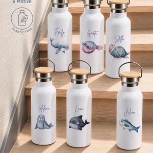 May include: Six white metal water bottles with bamboo lids and metal handles. Each bottle features a unique watercolor sea creature illustration and a personalized name in cursive script. Text on the image reads: personalisiert 6 Motive PLASTIC FREE.