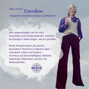 May include: A person with short gray hair wearing a purple long-sleeved blouse, a beige knit vest, and dark maroon wide-leg trousers. The person holds a white mug. Text on the image includes 'Hallo, ich bin Caroline' and 'MADE WITH LOVE'.
