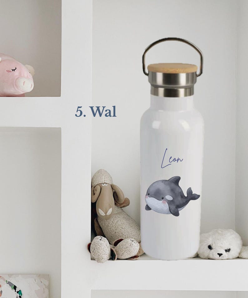 May include: A white water bottle with a silver metal neck and a light brown wooden lid featuring a metal handle. The bottle displays a graphic of a gray and white whale with the name Leon written in blue script above the whale illustration.