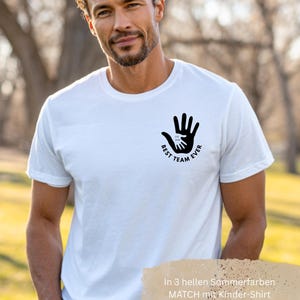 Puede incluir: Camiseta blanca con un gr&aacute;fico negro de dos manos, una dentro de la otra, y el texto "BEST TEAM EVER". La camiseta est&aacute; hecha de un material suave.