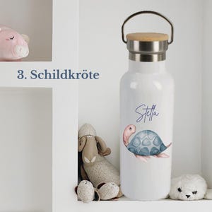 May include: A white water bottle with a metal handle and a wooden lid. The bottle features a watercolor illustration of a blue and pink turtle and the name Stella written in blue script. The text 3. Schildkr&ouml;te is visible to the left.