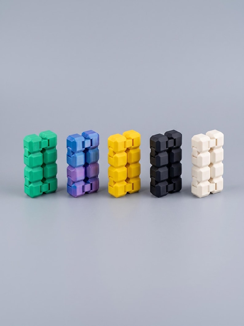 Puede incluir: Cinco juguetes fidget rectangulares dispuestos en fila, cada uno compuesto por m&uacute;ltiples segmentos interconectados en forma de cubo. Los colores de izquierda a derecha son verde s&oacute;lido, un degradado p&uacute;rpura y azul, amarillo s&oacute;lido, negro s&oacute;lido y blanco hueso.