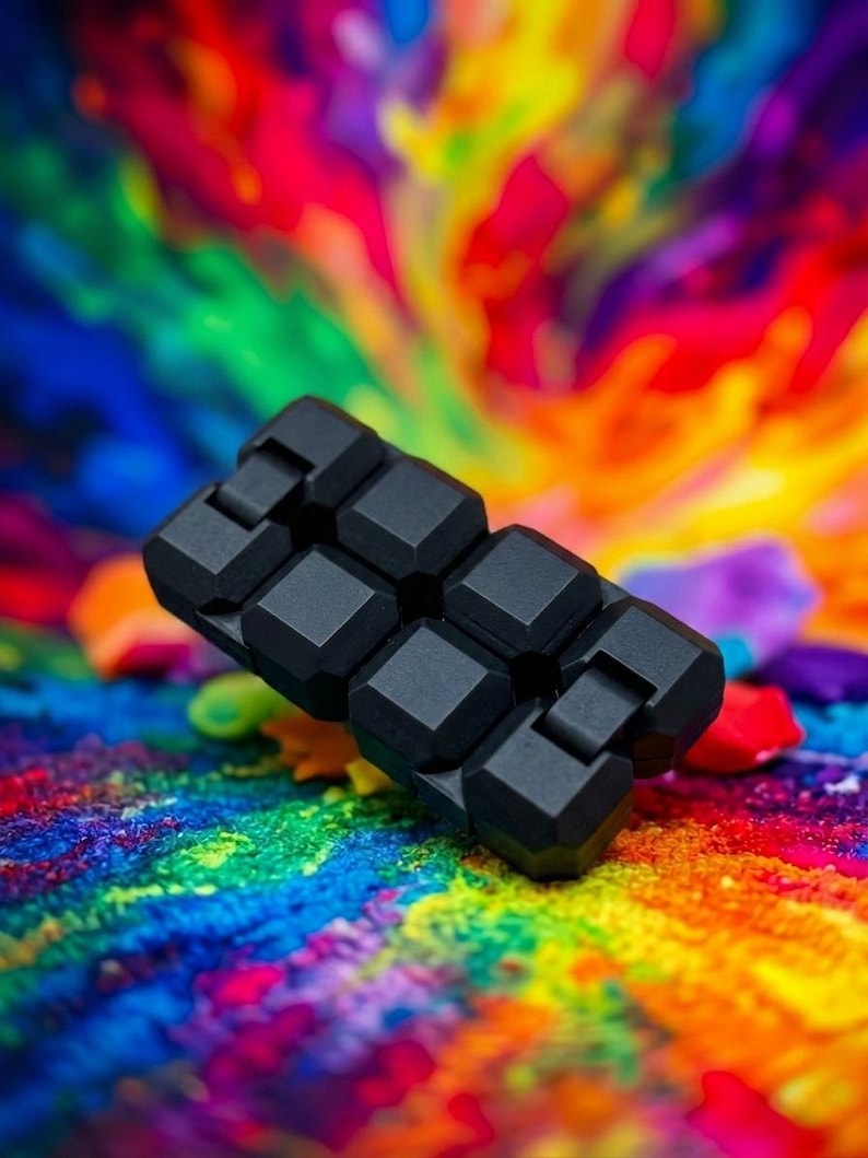Puede incluir: Un juguete antiestr&eacute;s negro compuesto por ocho cubos interconectados con acabado mate, dispuestos en un bloque rectangular. El objeto presenta un dise&ntilde;o segmentado con bisagras visibles entre cada cubo, lo que permite plegarlo y manipularlo.