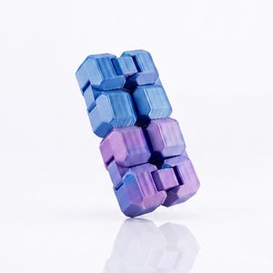 Pode incluir: Um brinquedo fidget composto por múltiplos segmentos interconectados em forma de bloco, dispostos numa formação retangular. O objeto apresenta um esquema de cores degradê que transita de um azul vibrante no topo para um roxo profundo na base.