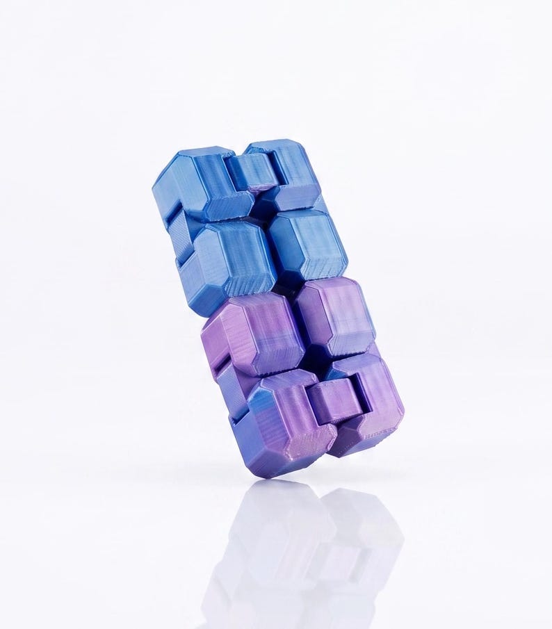 Puede incluir: Un juguete antiestr&eacute;s compuesto por m&uacute;ltiples segmentos interconectados en forma de bloque, dispuestos en una formaci&oacute;n rectangular. El objeto presenta un esquema de color degradado que va de un azul vibrante arriba a un morado intenso abajo.