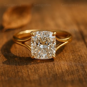 Könnte beinhalten: Ein goldener Ring mit einem großen, quadratisch geschliffenen Diamanten. Der Diamant ist klar und facettenreich und reflektiert das Licht. Der Ring hat ein schlichtes, elegantes Design.