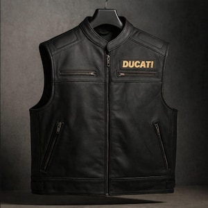 Può includere: Gilet in pelle nera con collo alto e chiusura a zip. Il gilet presenta due tasche sul petto con cerniera e due tasche inferiori con cerniera. La parola "DUCATI" è ricamata su una toppa sul petto. Il gilet è appeso a una gruccia nera.
