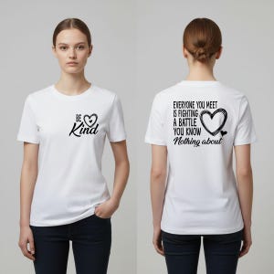 以下が含まれることがあります： 黒い文字とハートのグラフィックが入った白いTシャツ。「Be Kind」とハートのシンボルが前面にプリントされています。背面には「Everyone you meet is fighting a battle you know nothing about」とハートのグラフィックがプリントされています。
