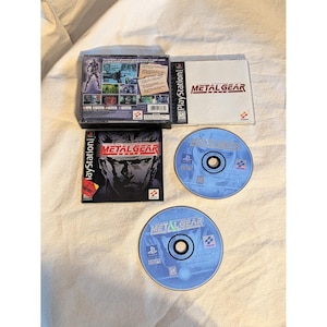 May include: Metal Gear video game for the PlayStation. The image shows the game case, disc, and instruction manual. The game case is black with the game title and character art. The disc is blue with the game title.