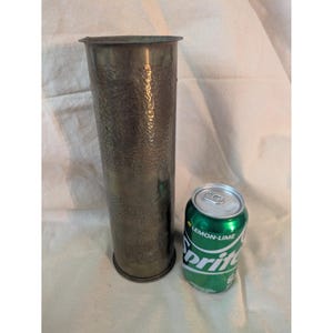 May include: A tall, hammered metal vase with a textured surface. The vase is cylindrical and has a dark, metallic finish. A green and white can of Sprite is next to the vase.