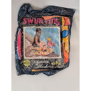 Op de afbeelding: Een verpakte opblaasbare zwemring in een donkere plastic zak. De verpakking bevat de tekst 'swim ring' en 'Inflatable', met een afbeelding van een persoon die een patroonrijke, veelkleurige opblaasbare ring gebruikt. Een gele cirkel toont 53x46 cm.