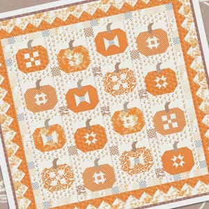 May include: A quilt pattern featuring a patchwork design of orange and cream pumpkins. The pattern is called "Pumpkins & Cream" and is by Fig Tree & Co.