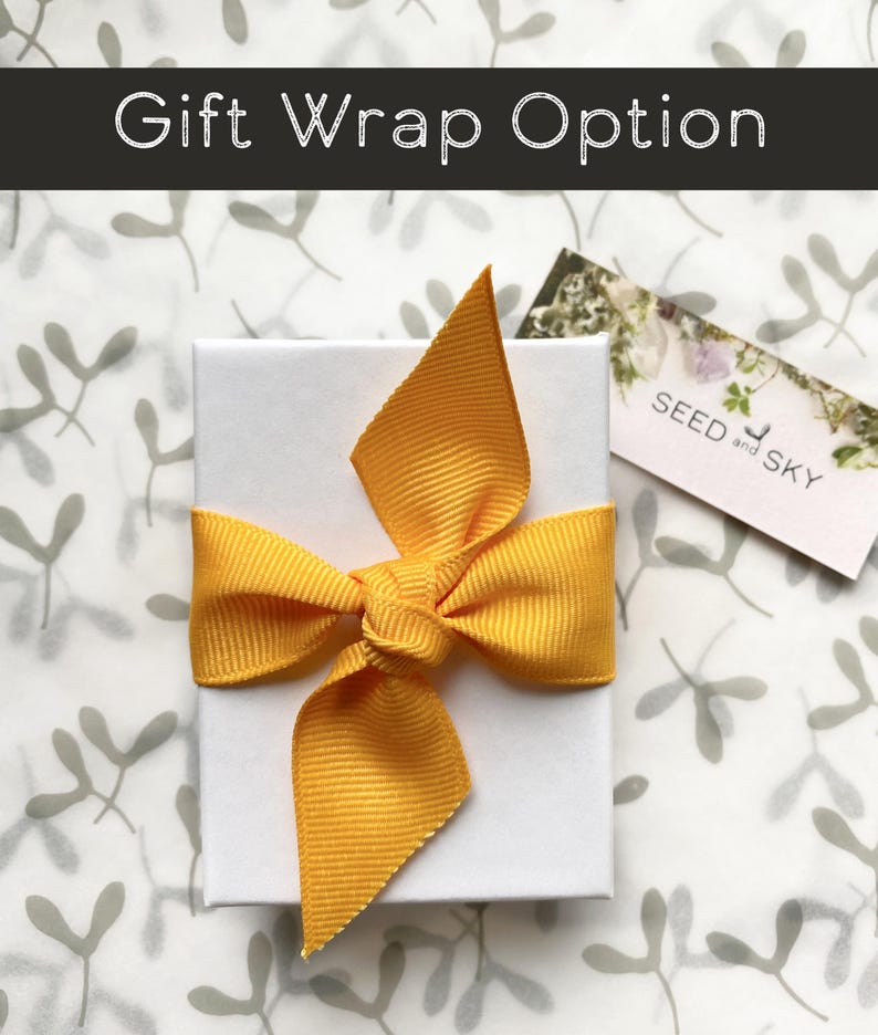 May include: A white gift box tied with a bright yellow ribbon. The box is on a patterned background with the text "Gift Wrap Option" at the top. A small tag with the text "SEED and SKY" is visible.